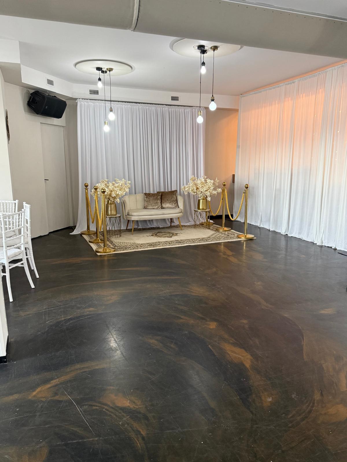 Trouwhoek met bankje, gordijnen en bloemstukken in de zaal van Tropicana Breda